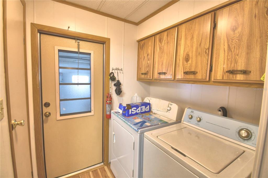 A laundry room features a white washer and dryer, wood cabinets, and a side door — 2055 S FLORAL AVENUE UNIT 119, BARTOW, FL