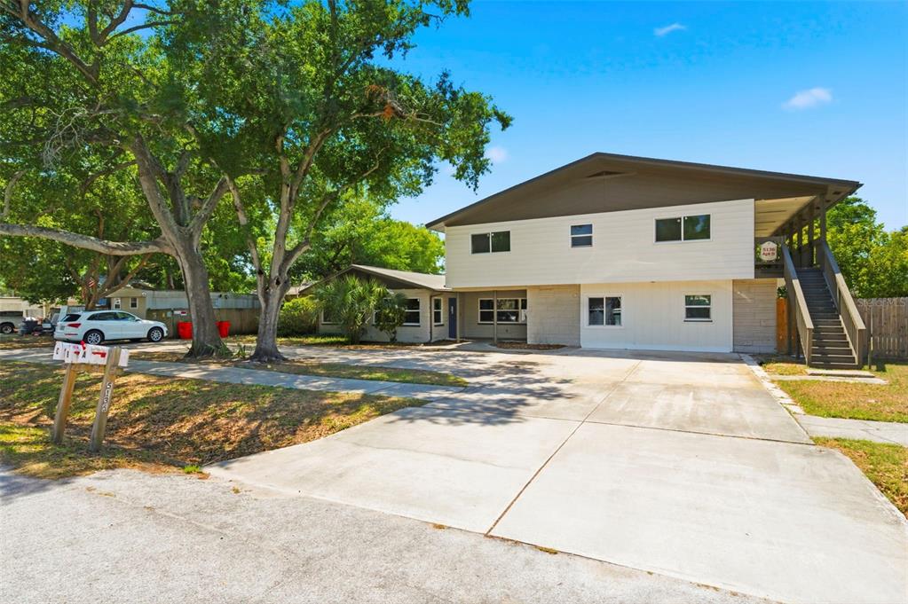 A two-story multi-family building with a concrete driveway, large trees, and an exterior staircase — 5136 68TH STREET N, ST PETERSBURG, FL
