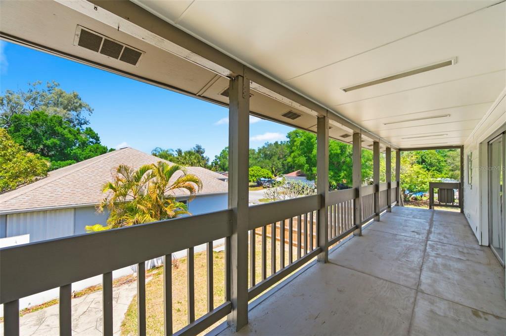 A covered outdoor balcony features a concrete floor, wooden railings, and views of nearby trees — 5136 68TH STREET N, ST PETERSBURG, FL