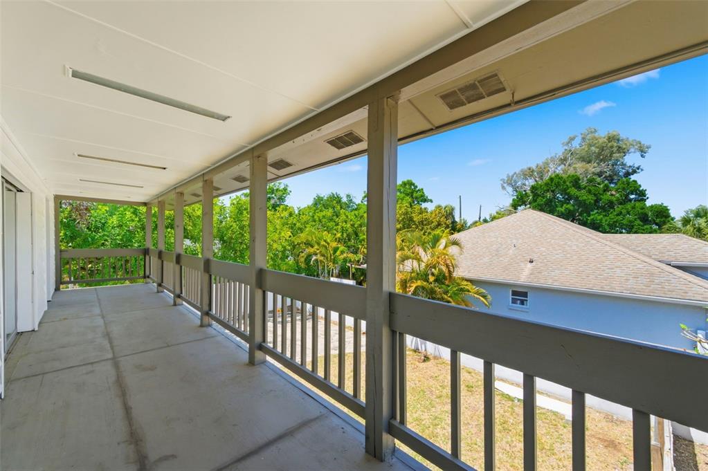 A covered outdoor balcony features a concrete floor and a wooden railing overlooking trees — 5136 68TH STREET N, ST PETERSBURG, FL