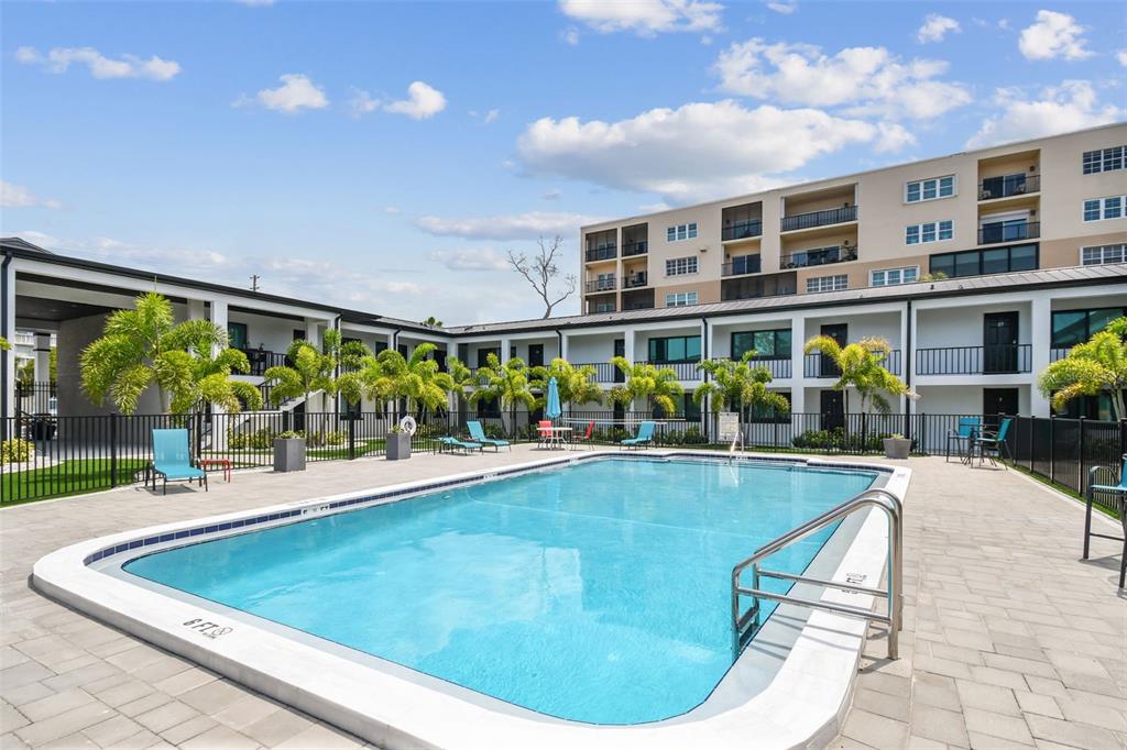 A rectangular swimming pool sits in a paved courtyard surrounded by a multi-story apartment building — 2942 W BAY DRIVE UNIT 24, BELLEAIR BLUFFS, FL