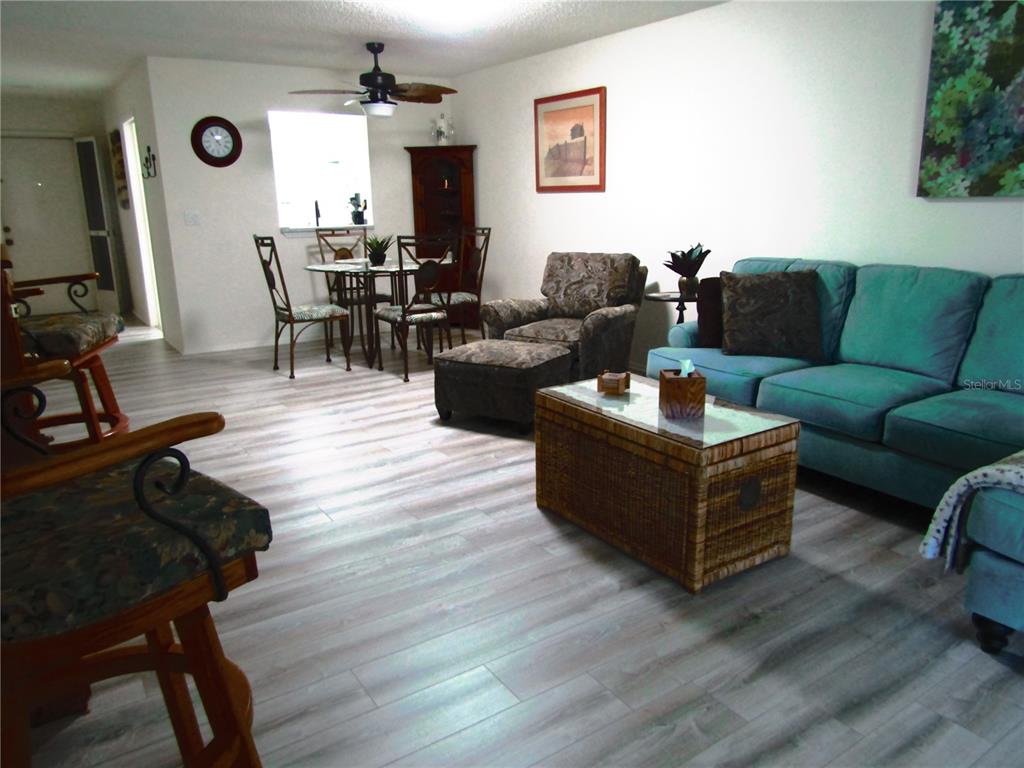 A living room and dining area with light wood-look flooring and a teal sofa — 7050 W COUNTRY CLUB DRIVE N UNIT 10-A, SARASOTA, FL