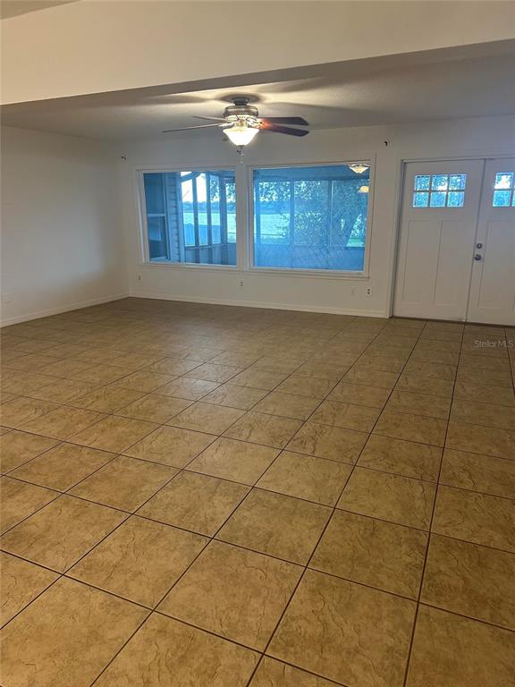 An open room features tan tile flooring, a ceiling fan, and large windows overlooking water — 1512 ISON LANE, OCOEE, FL