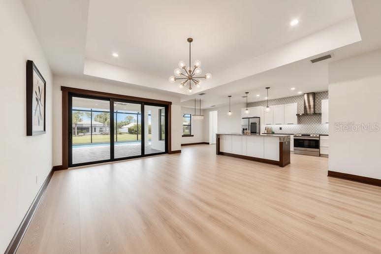 An open-concept living area features light wood flooring, a modern kitchen, and sliding glass doors — 5 MEDALIST CIRCLE, ROTONDA WEST, FL