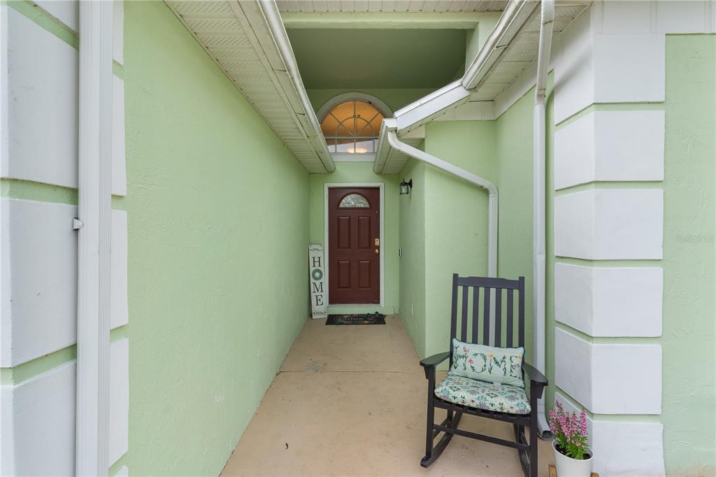 A covered entryway features a red front door, a rocking chair, and light green walls — 40045 PALM STREET, LADY LAKE, FL