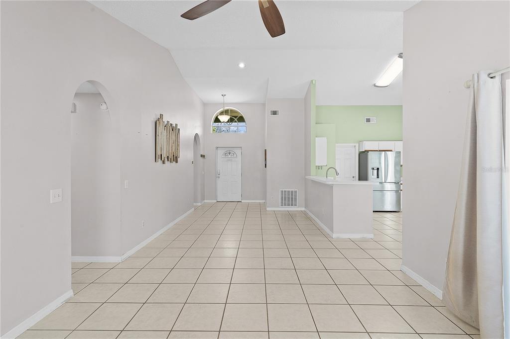 A bright, open-concept living area features light-colored tile flooring, vaulted ceilings, and an arched entryway — 40045 PALM STREET, LADY LAKE, FL