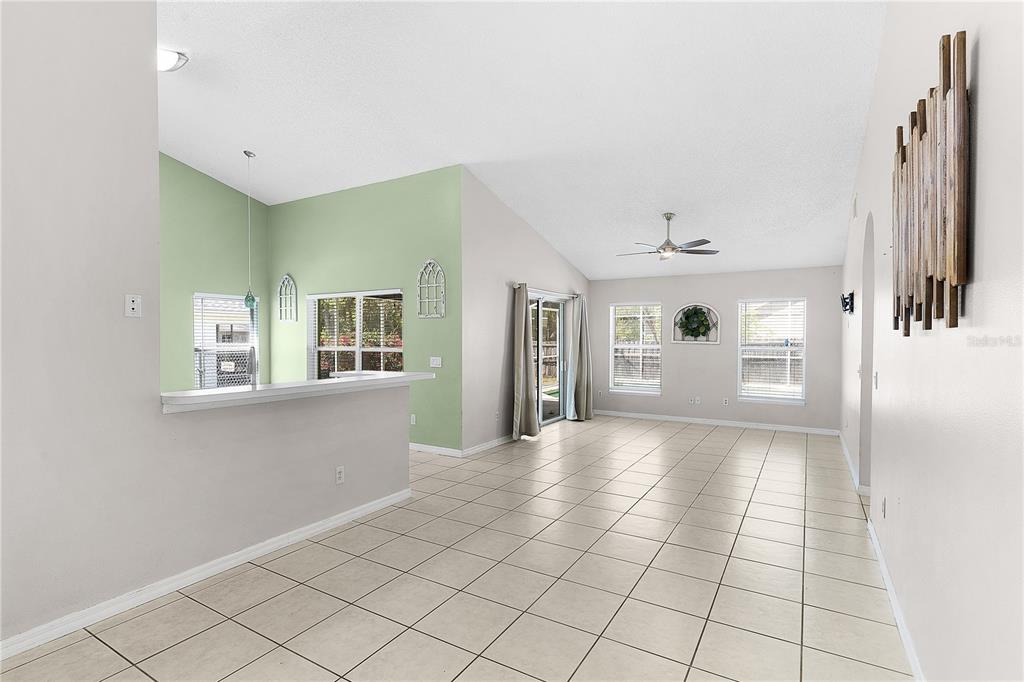 An open-concept living and dining area with light tile flooring, vaulted ceilings, and green walls — 40045 PALM STREET, LADY LAKE, FL