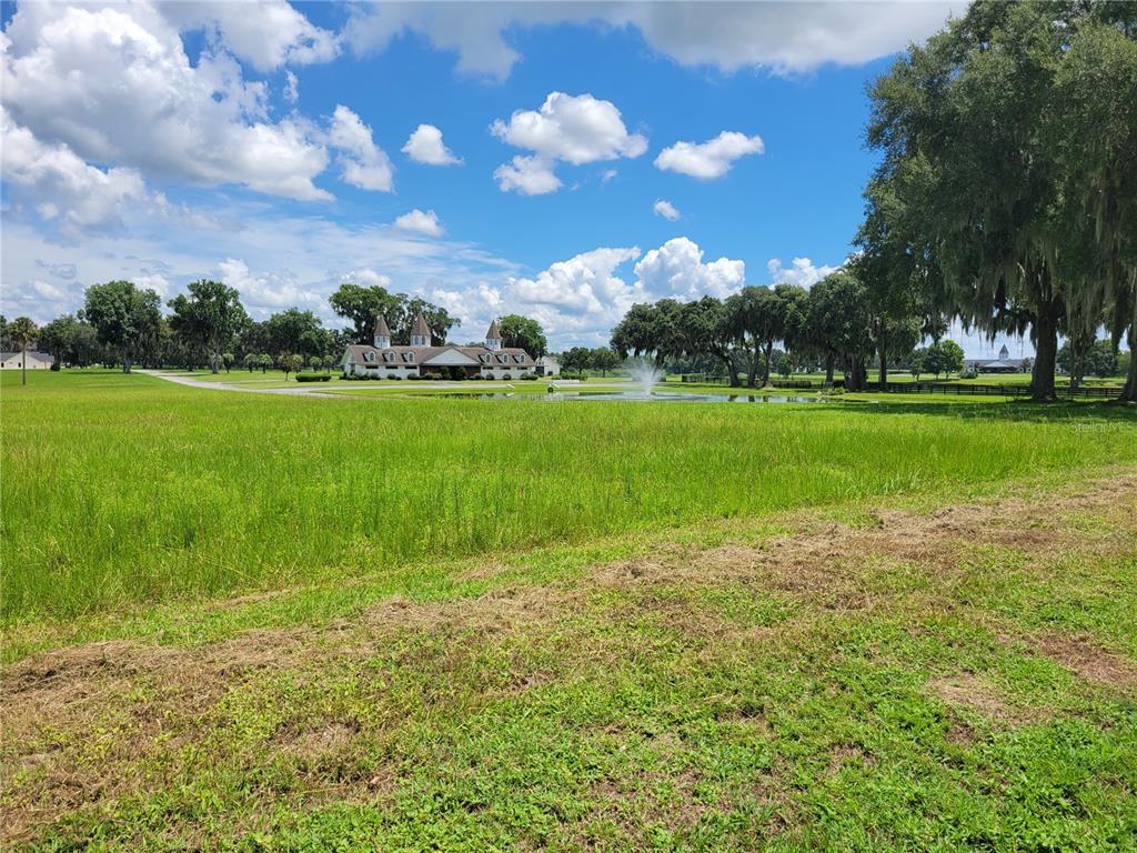 A large grassy field leads to a white building with turrets and a water fountain — 0 SE 61ST TERRACE ROAD UNIT 16, SUMMERFIELD, FL
