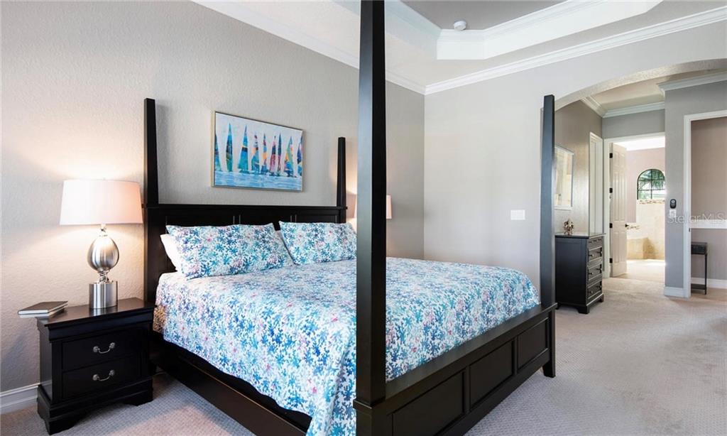 A bedroom features a dark wood four-poster bed, floral bedding, and a matching nightstand — 5543 ARNIE LOOP, BRADENTON, FL