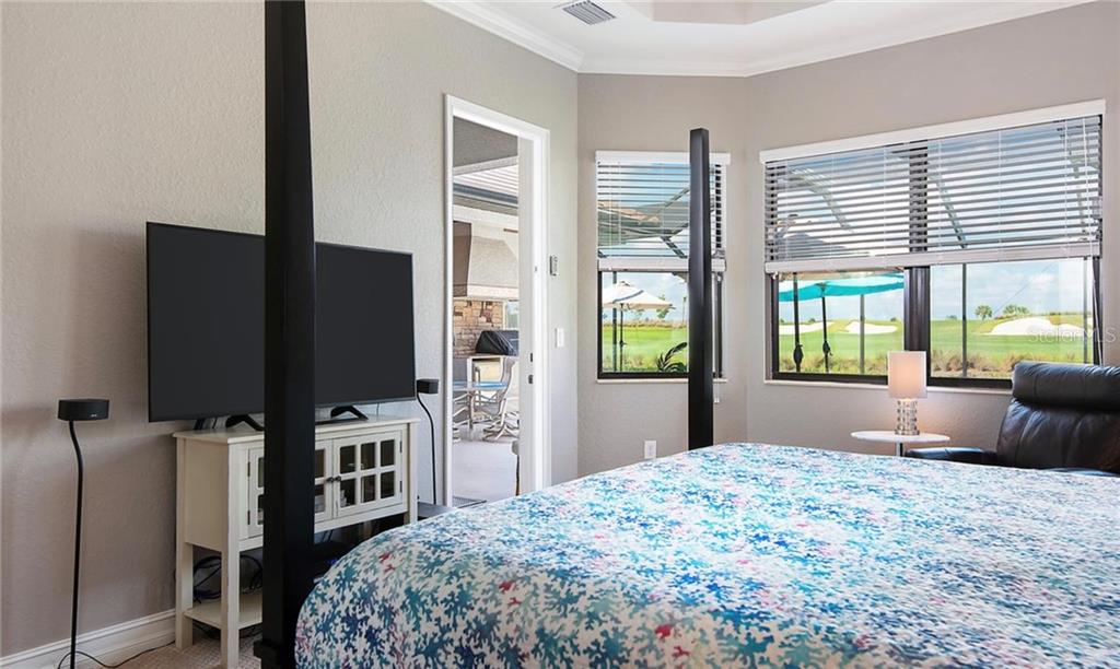 A bedroom with a four-poster bed, television, and a doorway leading to an outdoor patio — 5543 ARNIE LOOP, BRADENTON, FL