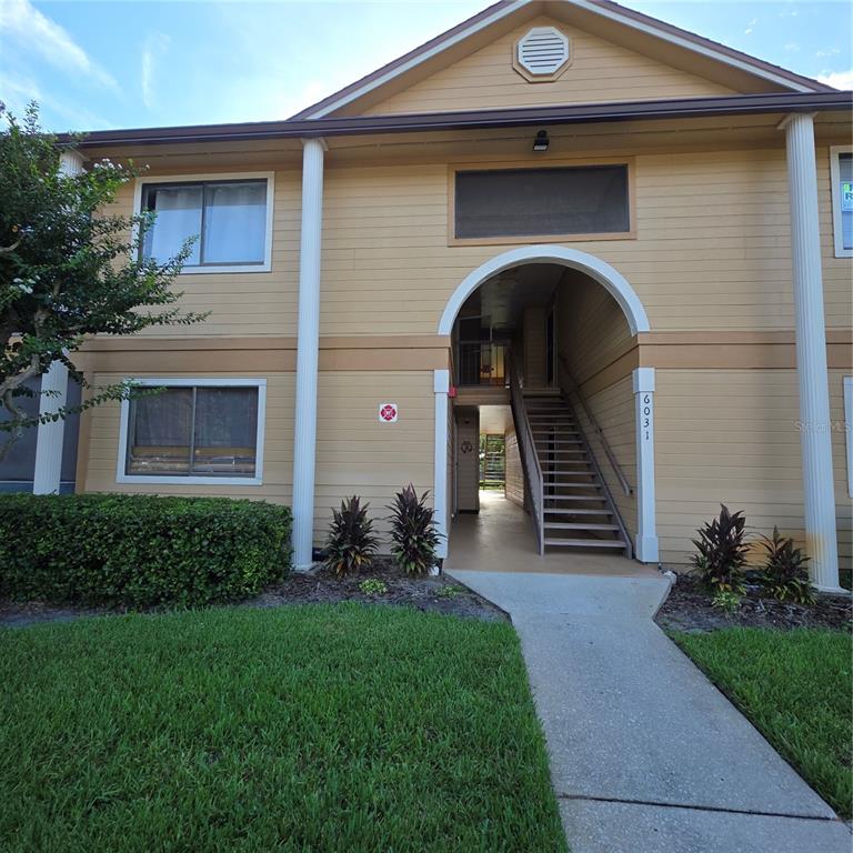 A two-story tan building exterior features vertical columns, horizontal siding, and multiple windows — 6031 SCOTCHWOOD GLEN UNIT 204, ORLANDO, FL