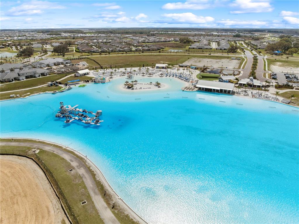 An aerial view shows a large turquoise swimming lagoon with an inflatable obstacle course — 31875 MAGNA GULF LOOP, SAN ANTONIO, FL