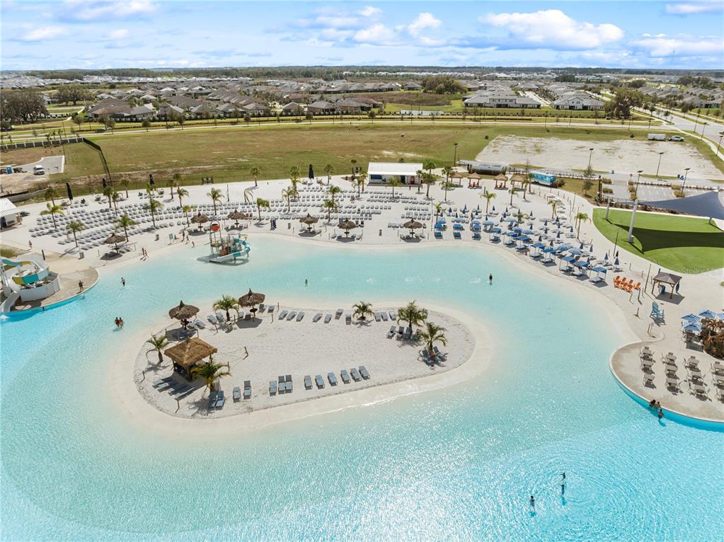An aerial view shows a large swimming lagoon with a central sandy island and lounge chairs — 31875 MAGNA GULF LOOP, SAN ANTONIO, FL
