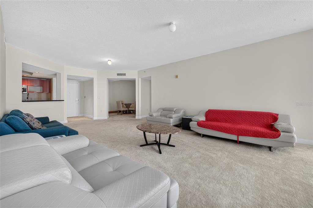 A spacious living room features beige carpeting, neutral walls, and multiple leather sofas — 241 RIVERSIDE DRIVE UNIT 907, HOLLY HILL, FL