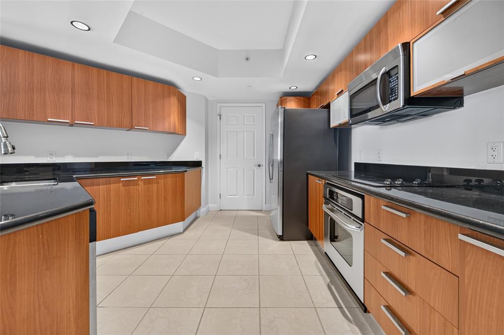 A kitchen features wood cabinets, black countertops, stainless steel appliances, and light tile flooring — 241 RIVERSIDE DRIVE UNIT 907, HOLLY HILL, FL