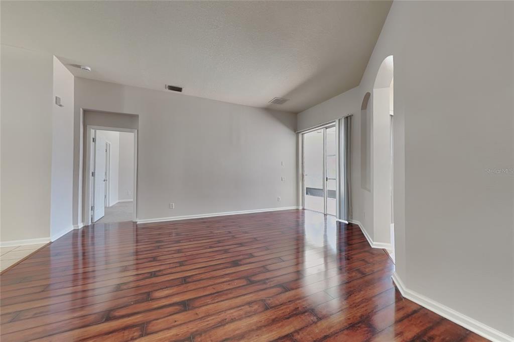 An empty living room features dark wood-look flooring, light gray walls, and sliding glass doors — 5714 99TH AVENUE CIRCLE E, PARRISH, FL