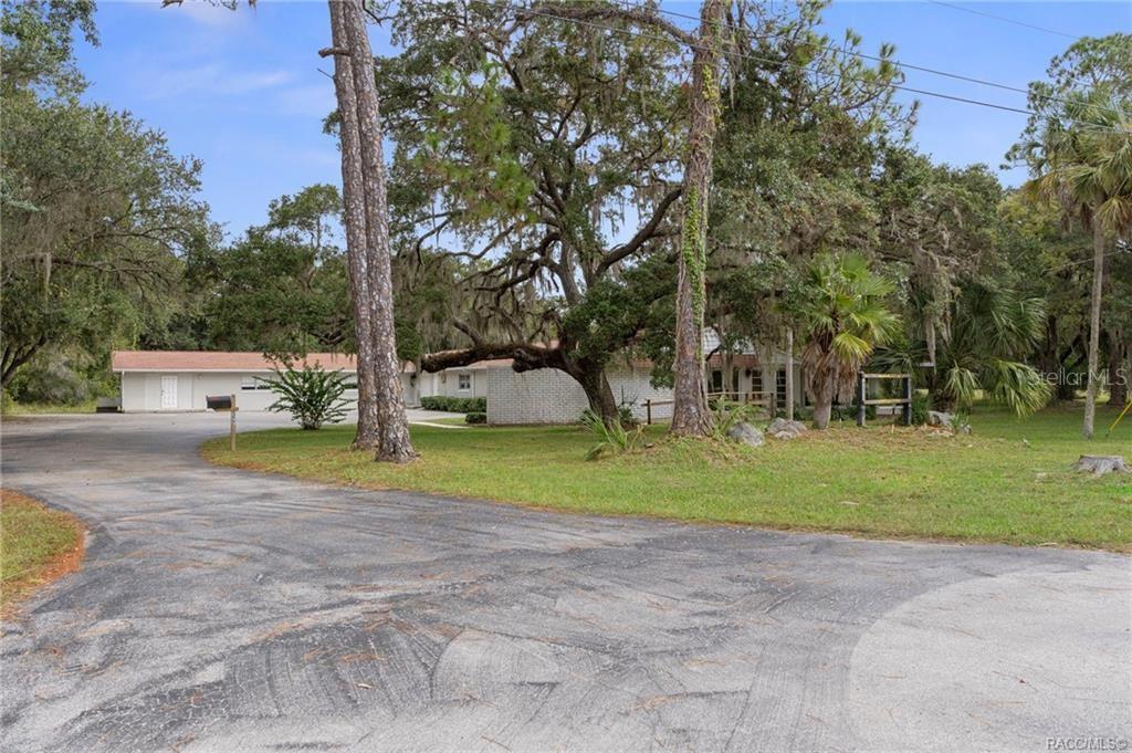 A paved driveway leads to a single-story house surrounded by large trees and grass — 377 HIGHWAY 40 W, INGLIS, FL