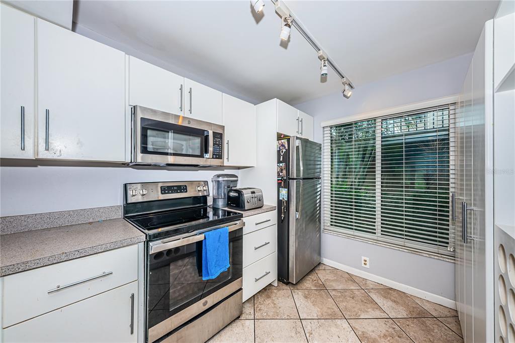 A kitchen features white cabinets, stainless steel appliances, a tiled floor, and a large window — 6269 PALMA DEL MAR BOULEVARD S UNIT 112, ST PETERSBURG, FL