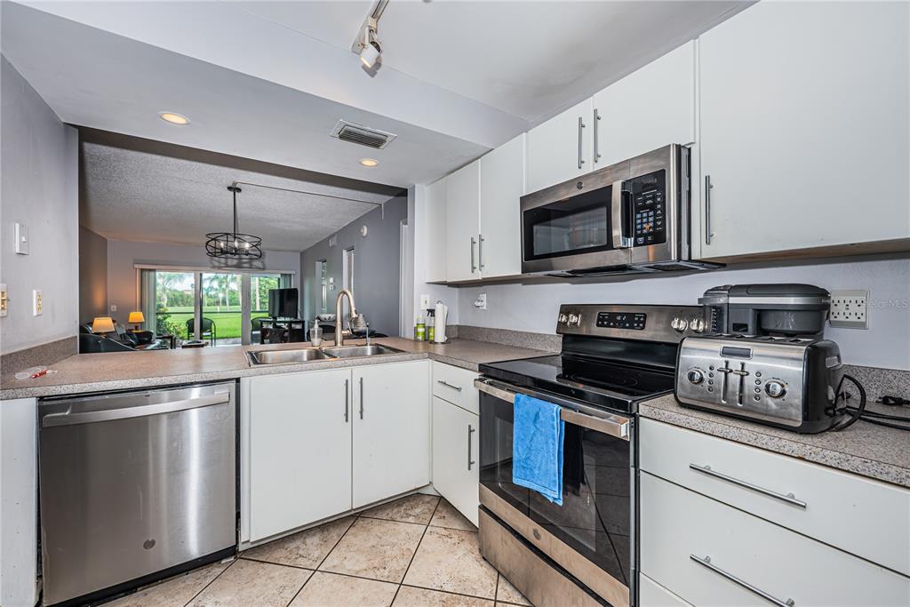 A kitchen with white cabinets, stainless steel appliances, and tile flooring opens to a living area — 6269 PALMA DEL MAR BOULEVARD S UNIT 112, ST PETERSBURG, FL