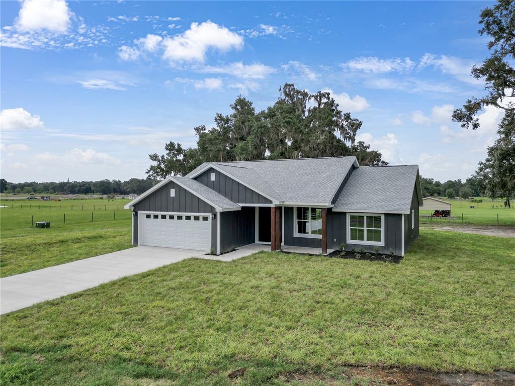 A dark gray, single-story house with a white garage door sits on a grassy lot — 1173 W C 476, BUSHNELL, FL