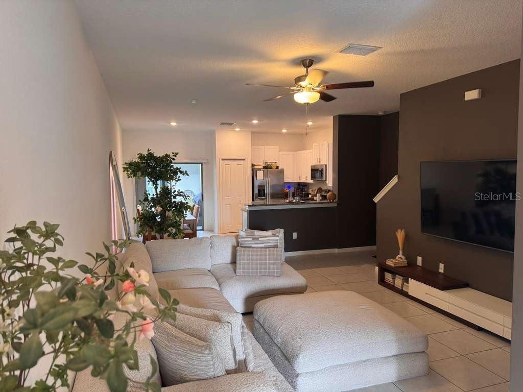 A living room with a sectional sofa, large television, and an open kitchen in the background — 8339 BIRCH HAVEN LANE, NEW PORT RICHEY, FL