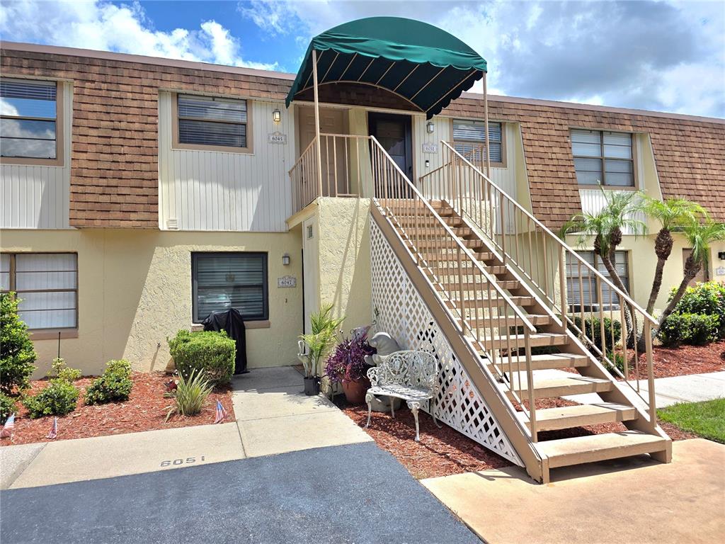 An exterior view of a two-story apartment building featuring a green awning and outdoor staircase — 6045 TOPHER TRAIL UNIT 24-C, MULBERRY, FL