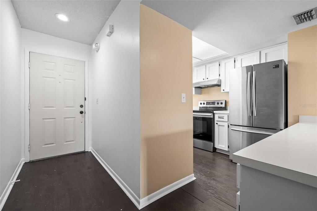 An entryway with dark flooring leads to a kitchen featuring white cabinets and stainless appliances — 6045 TOPHER TRAIL UNIT 24-C, MULBERRY, FL