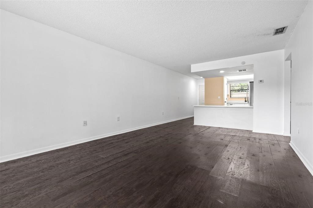 An empty living room with dark wood-look flooring and a pass-through kitchen counter — 6045 TOPHER TRAIL UNIT 24-C, MULBERRY, FL