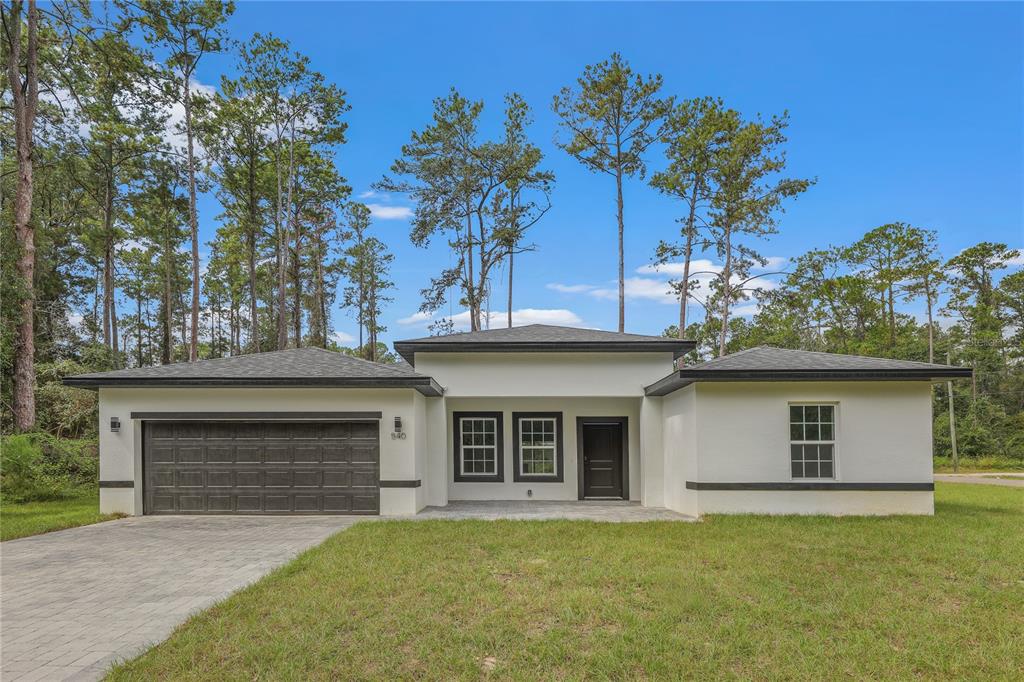 A single-story white house with a dark garage door and a paved driveway — 7833 SW 148TH STREET, OCALA, FL