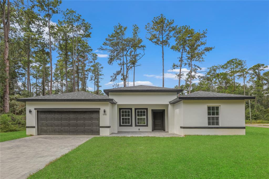 A single-story house with a white stucco exterior, a dark garage door, and a paved driveway — 7833 SW 148TH STREET, OCALA, FL