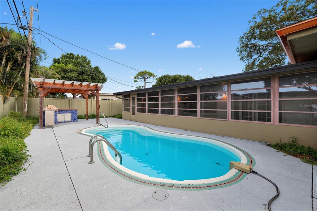 A backyard features a swimming pool, a wooden pergola, and a tiled outdoor kitchen area — 6450 31ST TERRACE N, ST PETERSBURG, FL