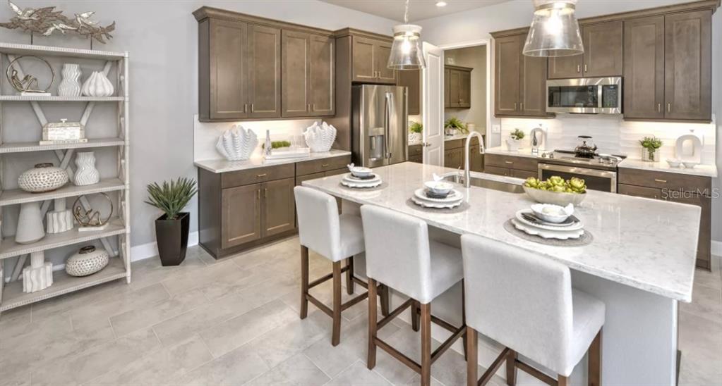 A kitchen features brown cabinets, a white quartz island with three stools, and tile flooring — 54 BRIGHTON LANE, ORMOND BEACH, FL