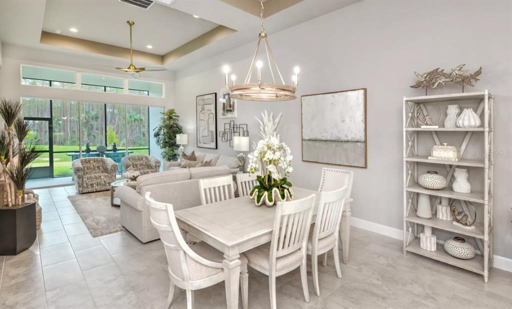 A dining area with a white table and chairs sits before a living room space — 54 BRIGHTON LANE, ORMOND BEACH, FL
