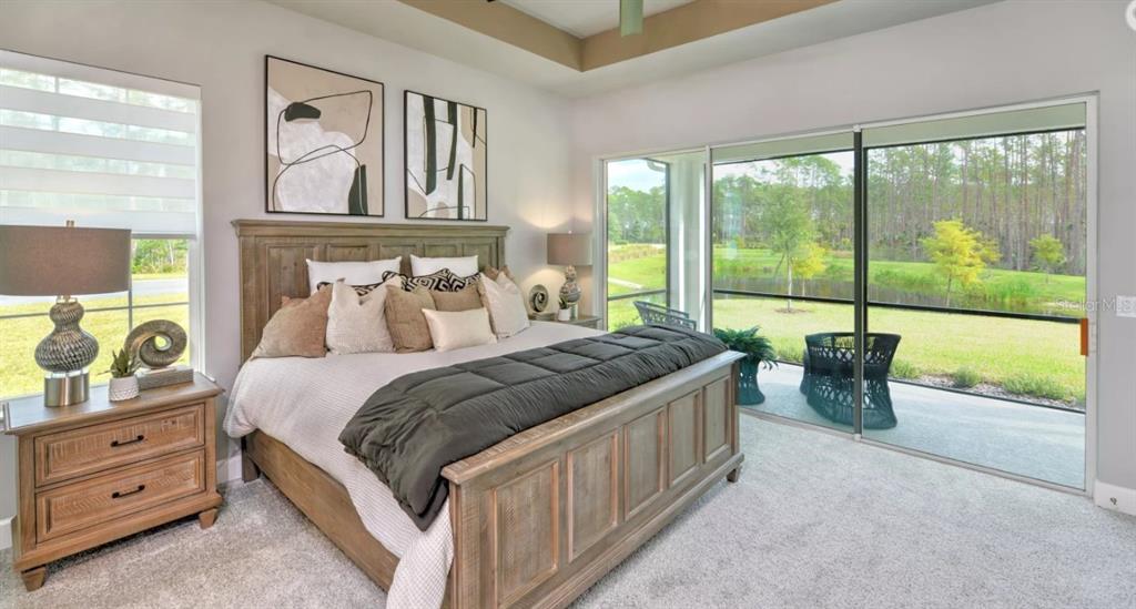 A bedroom features a wooden bed, nightstand, and sliding glass doors overlooking a grassy yard — 54 BRIGHTON LANE, ORMOND BEACH, FL