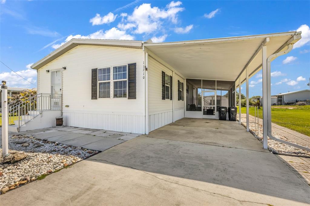 A white mobile home features a concrete driveway, a carport, and a screened-in porch area — 11710 SW ORANGE AVENUE, ARCADIA, FL