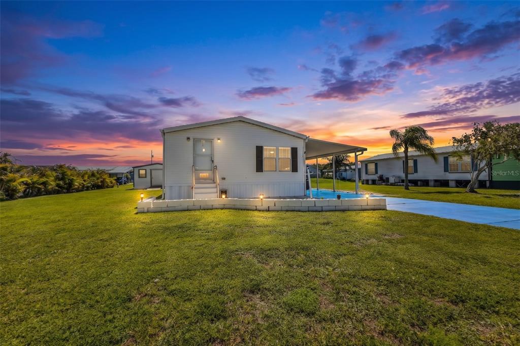 A single-story manufactured home with a white exterior and a small front patio at sunset — 11710 SW ORANGE AVENUE, ARCADIA, FL
