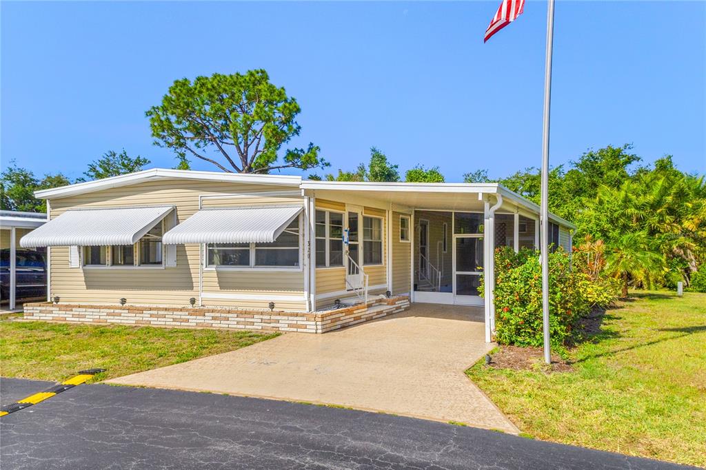 A tan mobile home features a concrete driveway, a screened porch, and a flag pole — 320 TROPIC DRIVE, OSPREY, FL