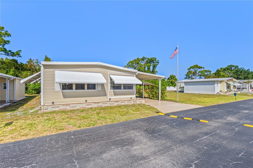 A tan mobile home with white awnings and a carport sits beside an asphalt road — 320 TROPIC DRIVE, OSPREY, FL