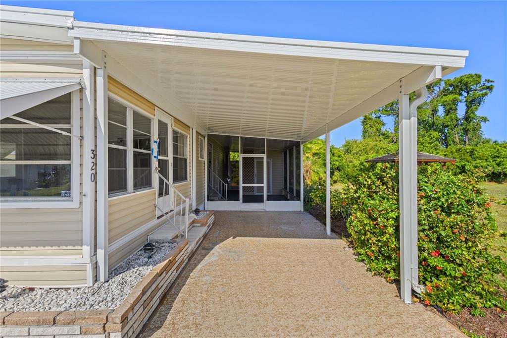 A covered carport leads to a screened-in porch entrance of a tan mobile home — 320 TROPIC DRIVE, OSPREY, FL