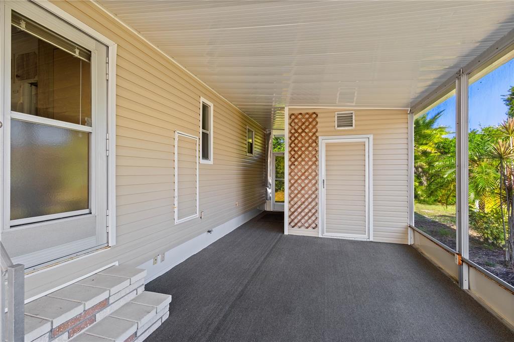 A covered porch with beige vinyl siding, a screened wall, and a gray carpeted floor — 320 TROPIC DRIVE, OSPREY, FL