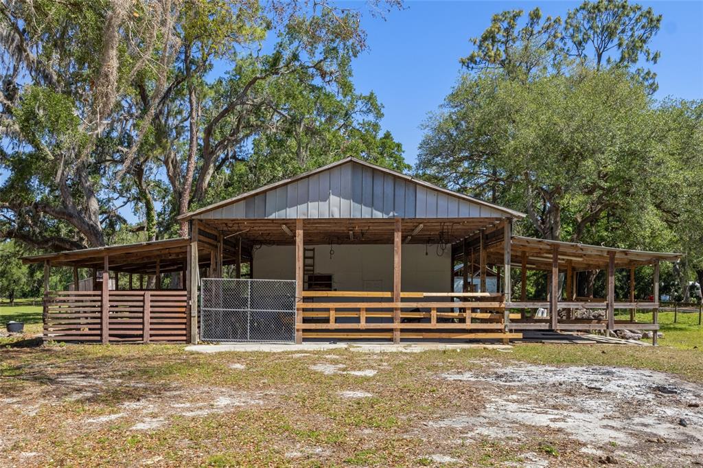 A metal-roofed barn with open-air stalls and a chain-link gate stands in a grassy field — 11902 CR 727, WEBSTER, FL