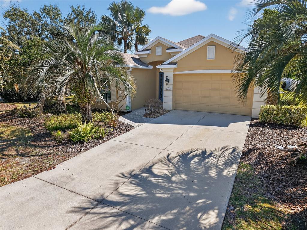A single-story house with a tan stucco exterior, a two-car garage, and palm trees — 8124 TABBYSTONE PLACE, BRADENTON, FL