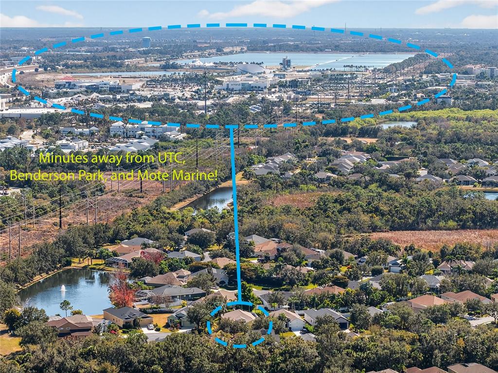 An aerial view shows a residential neighborhood with a lake and a distant shopping center — 8124 TABBYSTONE PLACE, BRADENTON, FL