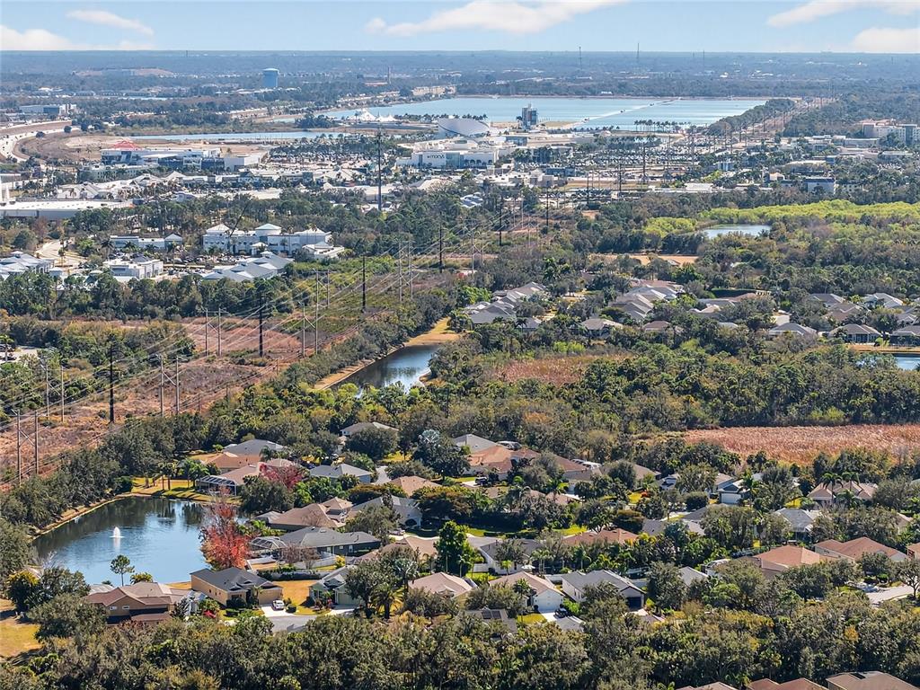 An aerial view shows a suburban neighborhood with houses, a pond, and a distant shopping center — 8124 TABBYSTONE PLACE, BRADENTON, FL
