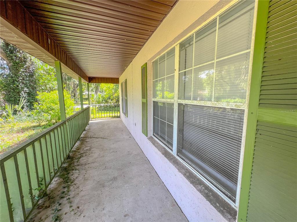 A covered concrete porch features green railings and shutters along the side of a house — 24535 NW 189TH AVENUE, HIGH SPRINGS, FL
