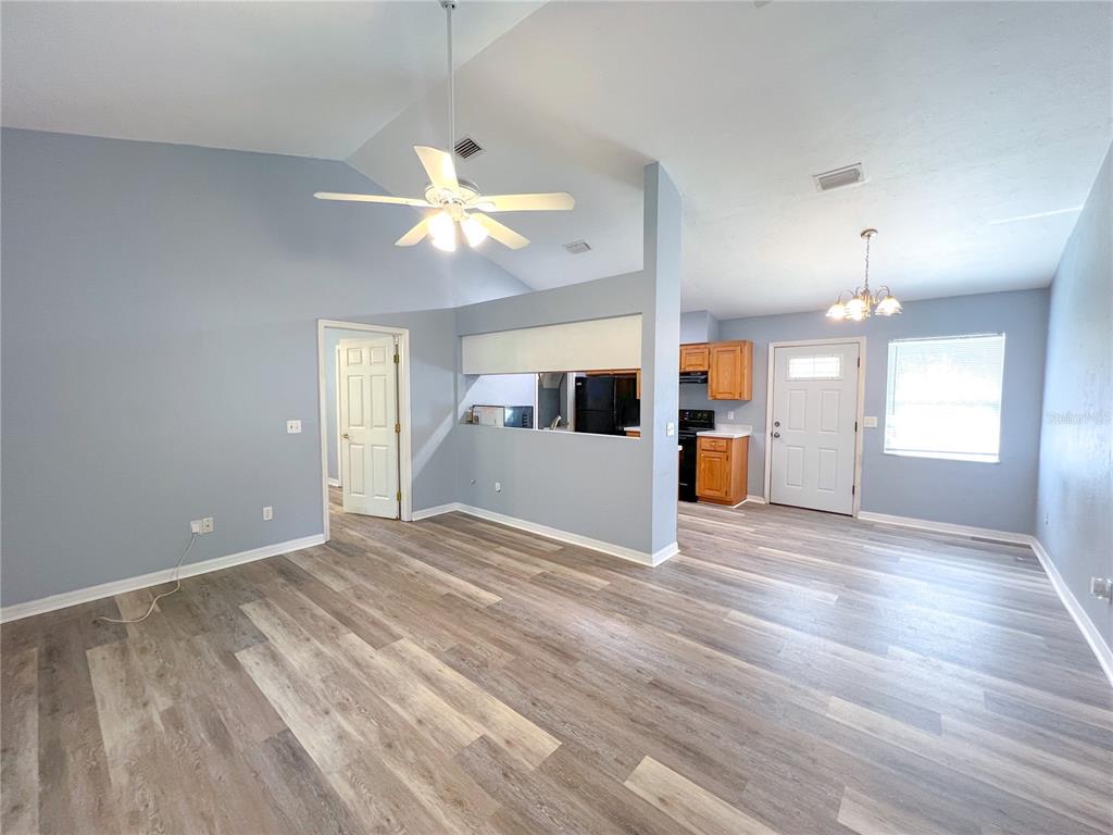 A living room with vaulted ceilings, light blue walls, and wood-look flooring opens to a kitchen — 24535 NW 189TH AVENUE, HIGH SPRINGS, FL