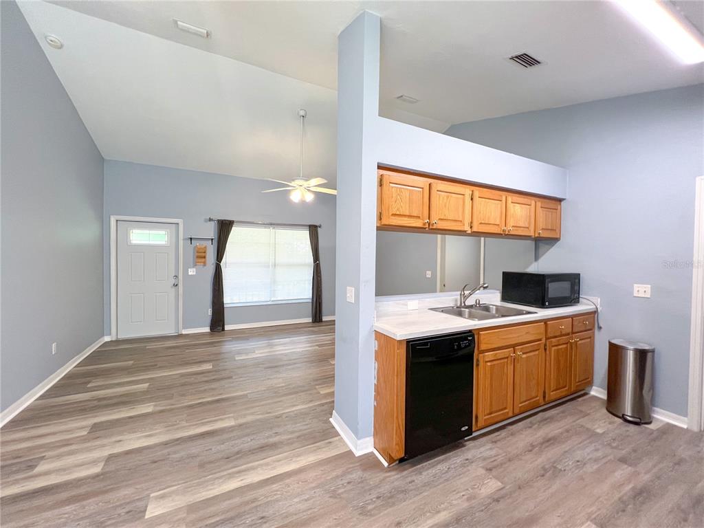 A kitchen with wood cabinets and a dishwasher opens into a living area with flooring — 24535 NW 189TH AVENUE, HIGH SPRINGS, FL