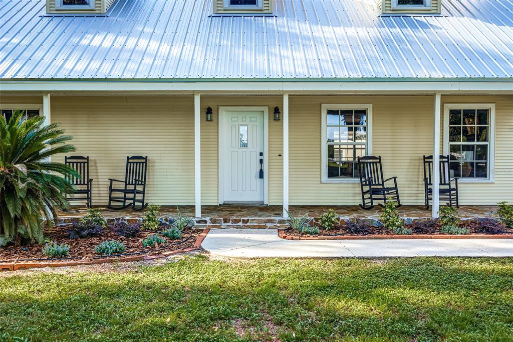 The front exterior of a house features a metal roof, porch with rocking chairs, and landscaping — 3501 E TRAPNELL ROAD, PLANT CITY, FL