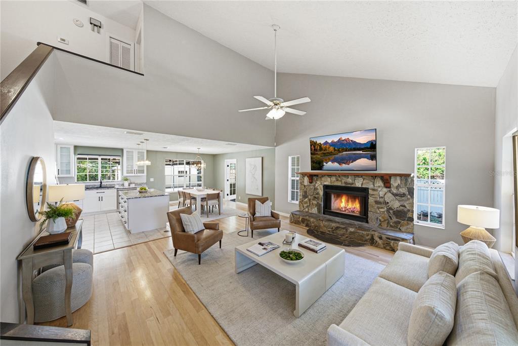 An open-concept living room and kitchen featuring a stone fireplace, vaulted ceilings, and hardwood floors — 3501 E TRAPNELL ROAD, PLANT CITY, FL
