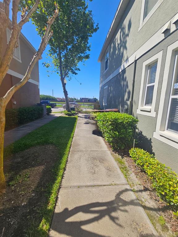 A concrete walkway runs between two residential buildings with green lawns and manicured hedges — 1917 ESTANCIA CIRCLE, KISSIMMEE, FL